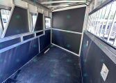 Interior of a metal trailer with black partition panels and aluminum framing, viewed from the doorway to the back end, near the windows on the right side
