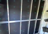 Interior of a cargo trailer with tall vertical black panels framed by silver metal; hooks along the top rail and an empty storage compartment along the wall.