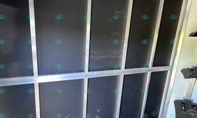 Interior of a cargo trailer with tall vertical black panels framed by silver metal; hooks along the top rail and an empty storage compartment along the wall.