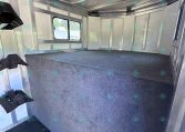Interior of an empty aluminum cargo trailer with a gray carpeted floor, metal sidewalls and a window along one wall