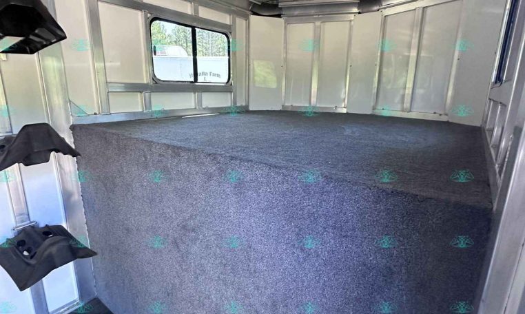 Interior of an empty aluminum cargo trailer with a gray carpeted floor, metal sidewalls and a window along one wall