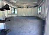 Interior of empty aluminum trailer with gray carpeted floor, side windows, and vertical wall ribs in sight.