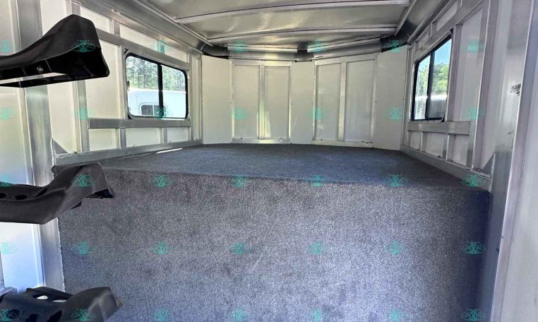 Interior of empty aluminum trailer with gray carpeted floor, side windows, and vertical wall ribs in sight.