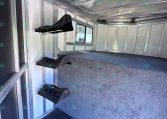 Interior of a aluminum horse trailer with wall-mounted saddle racks and a window at the far end.