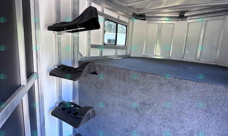 Interior of a aluminum horse trailer with wall-mounted saddle racks and a window at the far end.
