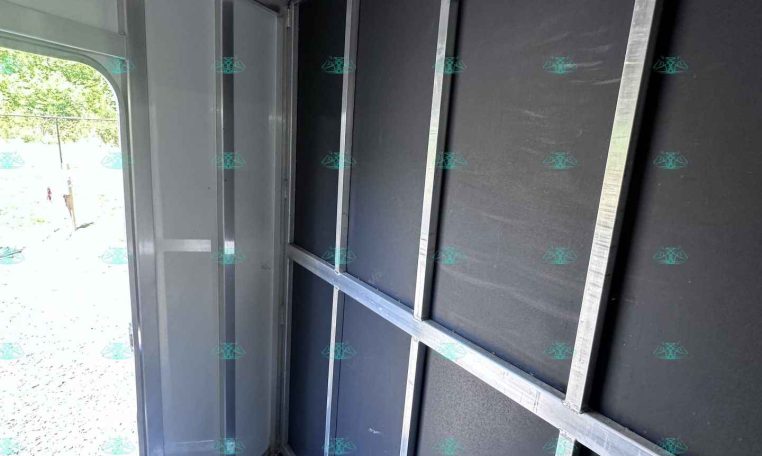 Interior of a metal trailer showing black wall panels and silver framing with ceiling hooks along the top edge.
